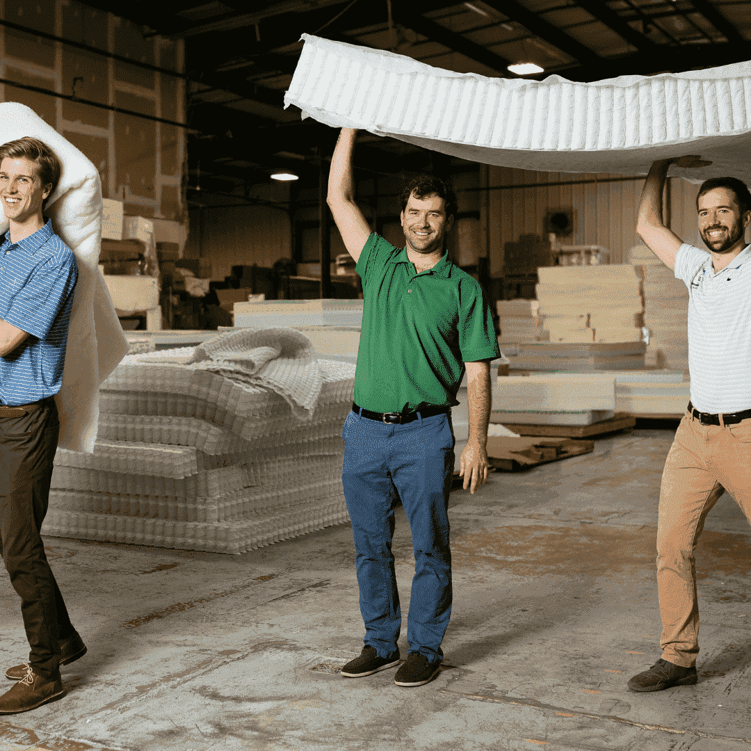 guys holding up a mattress smiling