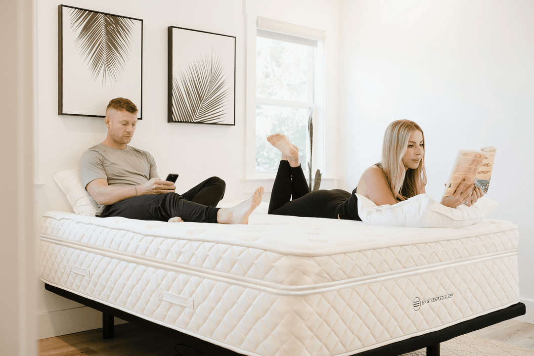 a couple laying in bed reading on an engineered sleep mattress