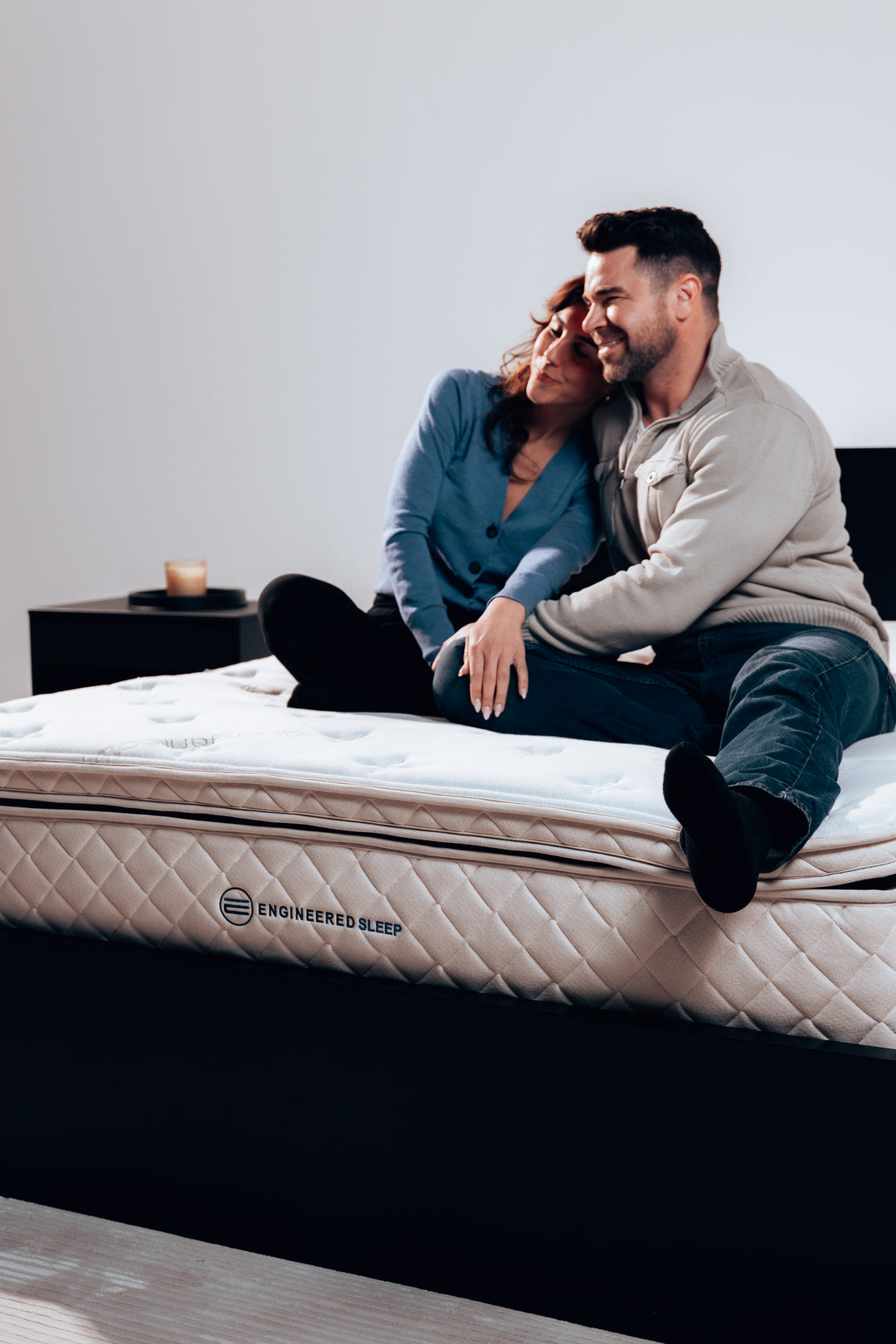 a man and a woman sitting on our DUO Mattress and smiling