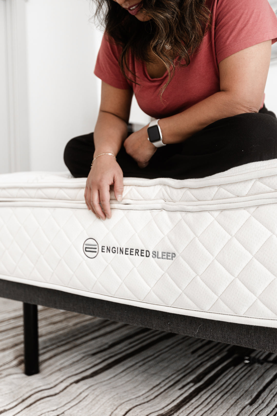 a woman sitting on the edge of our DUO Latex and showing how sturdy the edge support is on the mattress. Some of the best edge support you will find in a mattress.