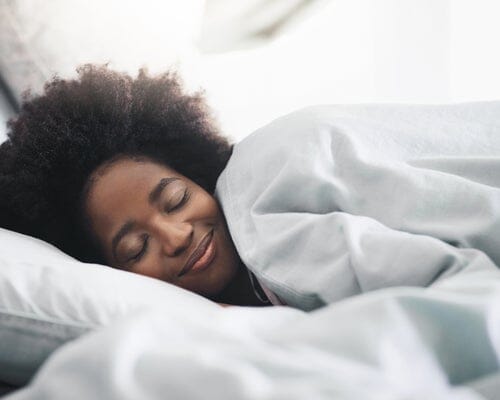 woman laying in bed smiling and comfortable in her sheets